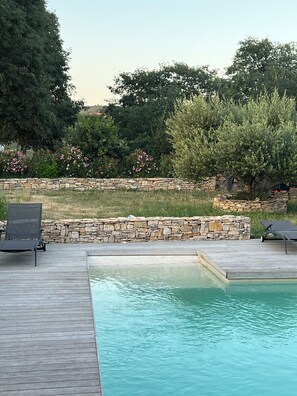 Ein Swimmingpool mit Holzterrasse, Steinmauer und Liegestühlen.