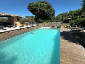 Una piscina rettangolare con acqua cristallina, circondata da un solarium in legno e dotata di lettini.
