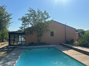 Ein Schwimmbecken mit Holzterrasse, einer gläsernen Struktur und einem Gebäude mit einem Fenster.