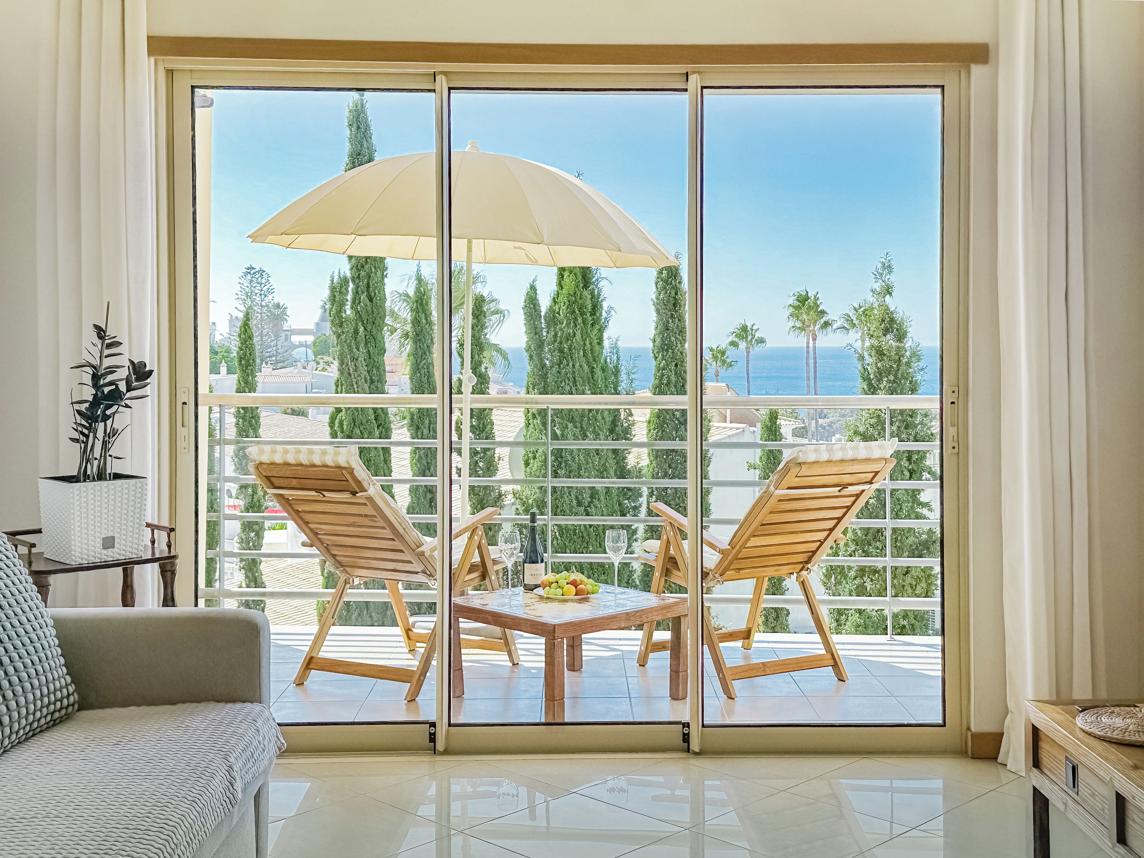 A balcony with two wooden chairs, a table with fruit, and a large umbrella.