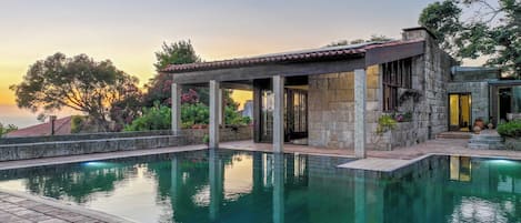 A poolside area with a stone building, a pergola, and a view of the sea.