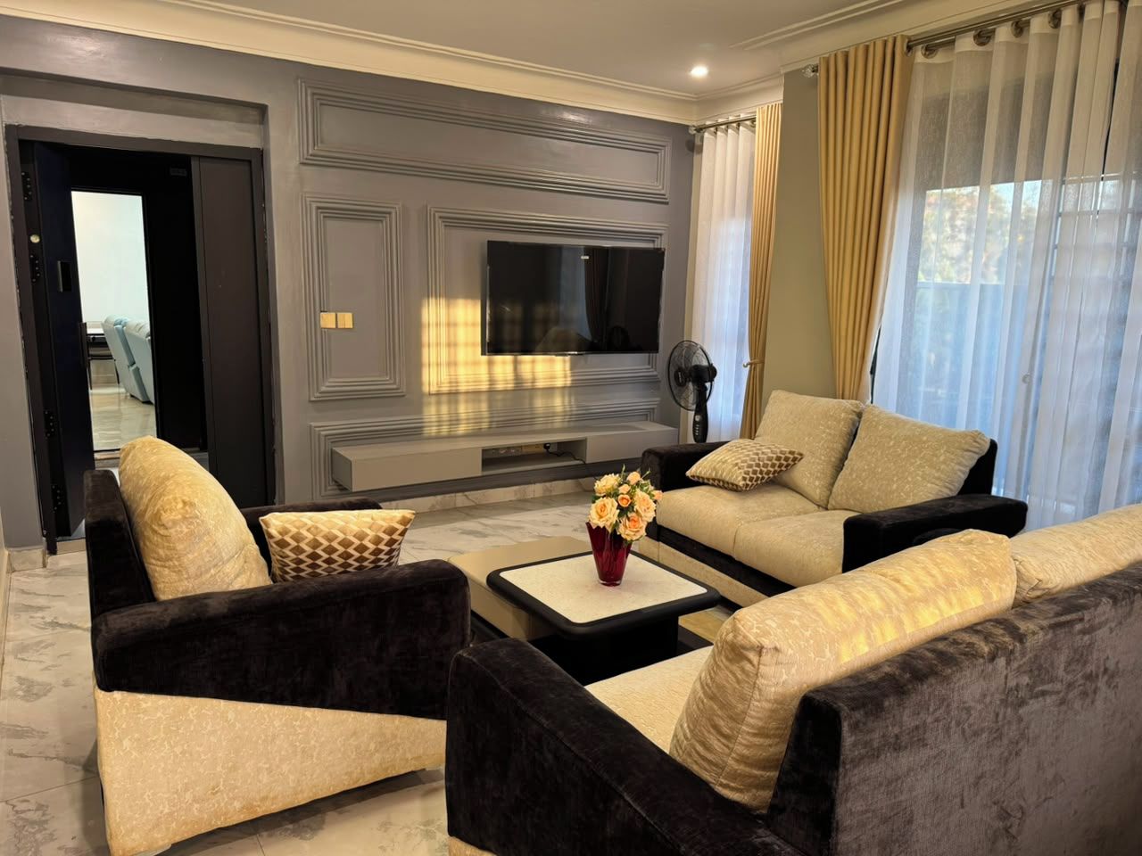 A modern living room with a flat-screen TV, two sofas, a coffee table, and a vase of flowers.