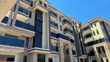 Un immeuble résidentiel à plusieurs étages, doté de balcons et d’une colonne centrale, avec un ciel dégagé.