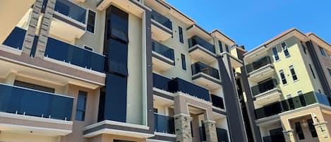 A multi-story residential building with balconies, a central column, and a clear sky.