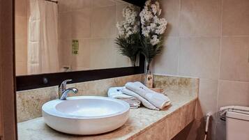 Un baño con un lavabo redondo, un espejo, un perchero para toallas y una planta en maceta.