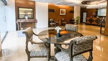 Un moderno vestíbulo de hotel con una mesa redonda de vidrio rodeada de sillones tapizados, una recepción y una chimenea.