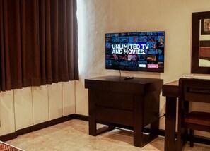 Una habitación con una televisión mostrando una selección de películas y programas de televisión, un mueble de madera oscura y una silla.