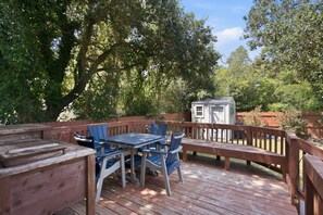 Eine Holzterrasse mit Tisch und Stühlen, umgeben von einem Holenzaun und Bäumen.