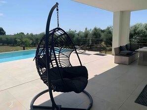 A hanging chair by a pool with a view of a garden and a patio area. - Holiday Home 'Aurora' with Private Pool, Wi-Fi and Air Conditioning (Marčana)