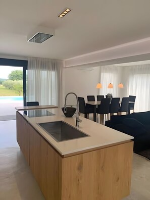 A modern kitchen with a central island, a dining area with chairs and a table, and a view of the outdoors. - Holiday Home 'Aurora' with Private Pool, Wi-Fi and Air Conditioning (Marčana)