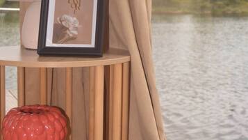 Una habitación con vista a un cuerpo de agua, un cuadro enmarcado, un florero rojo y una planta en maceta sobre una mesa de madera.