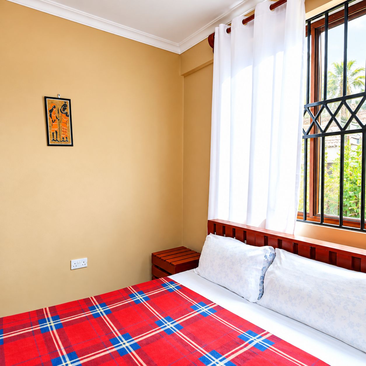 Une chambre à coucher comprenant un lit, une table de chevet, une fenêtre avec des rideaux et une prise de courant fixée au mur.