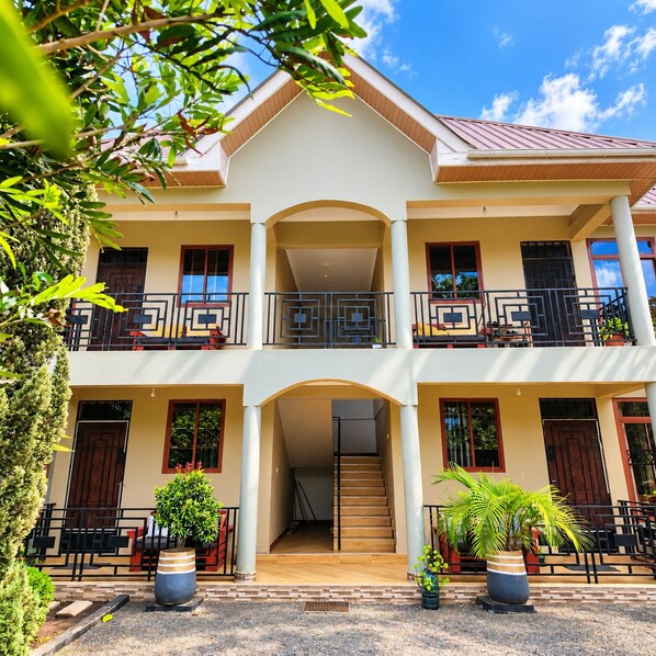 A two-story building with a central entrance, balconies on each floor, and potted plants in front.