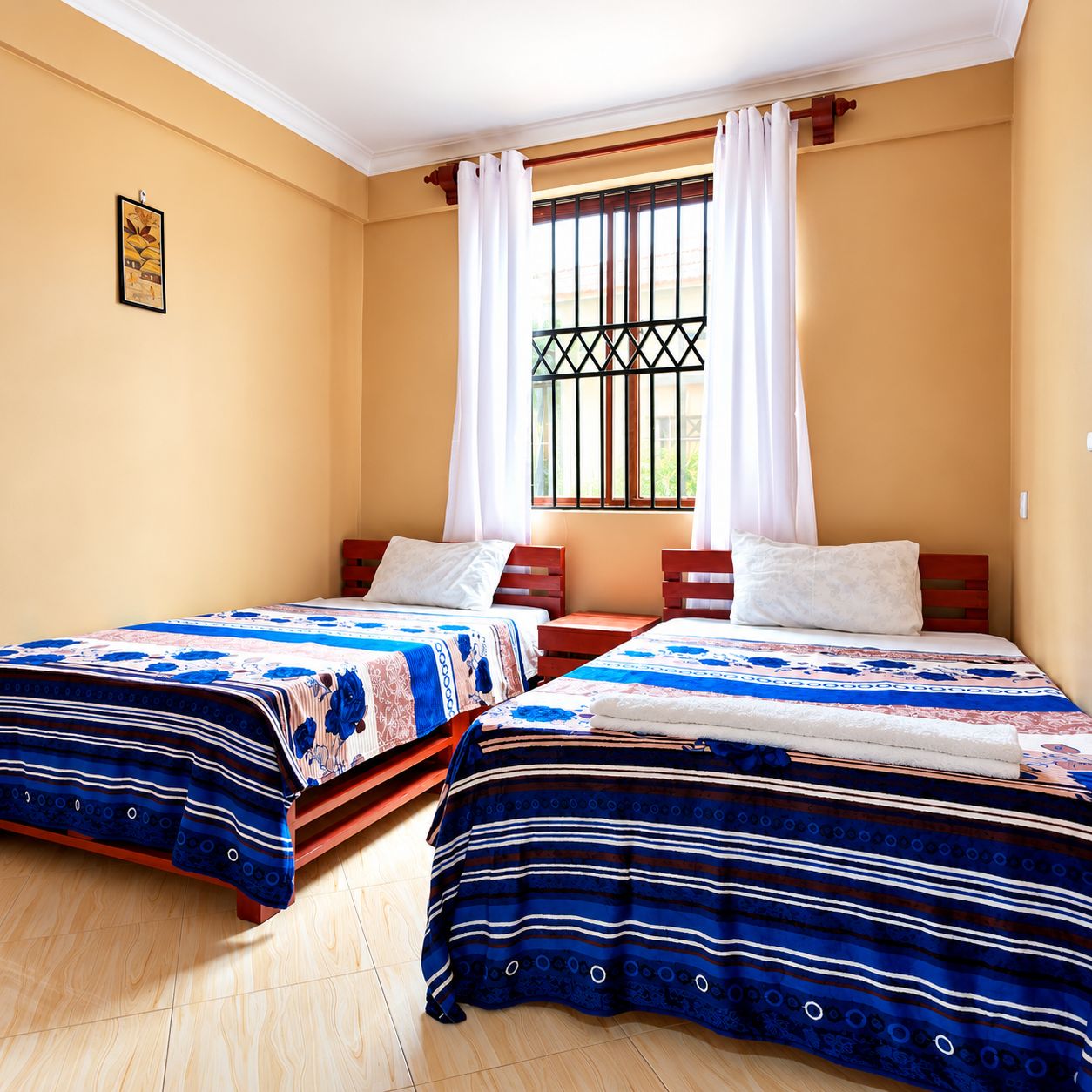 A room with two beds, a window with curtains, and a picture on the wall.
