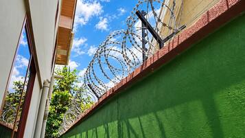 A narrow alleyway with a green wall and a barbed wire fence topped with a metal structure.