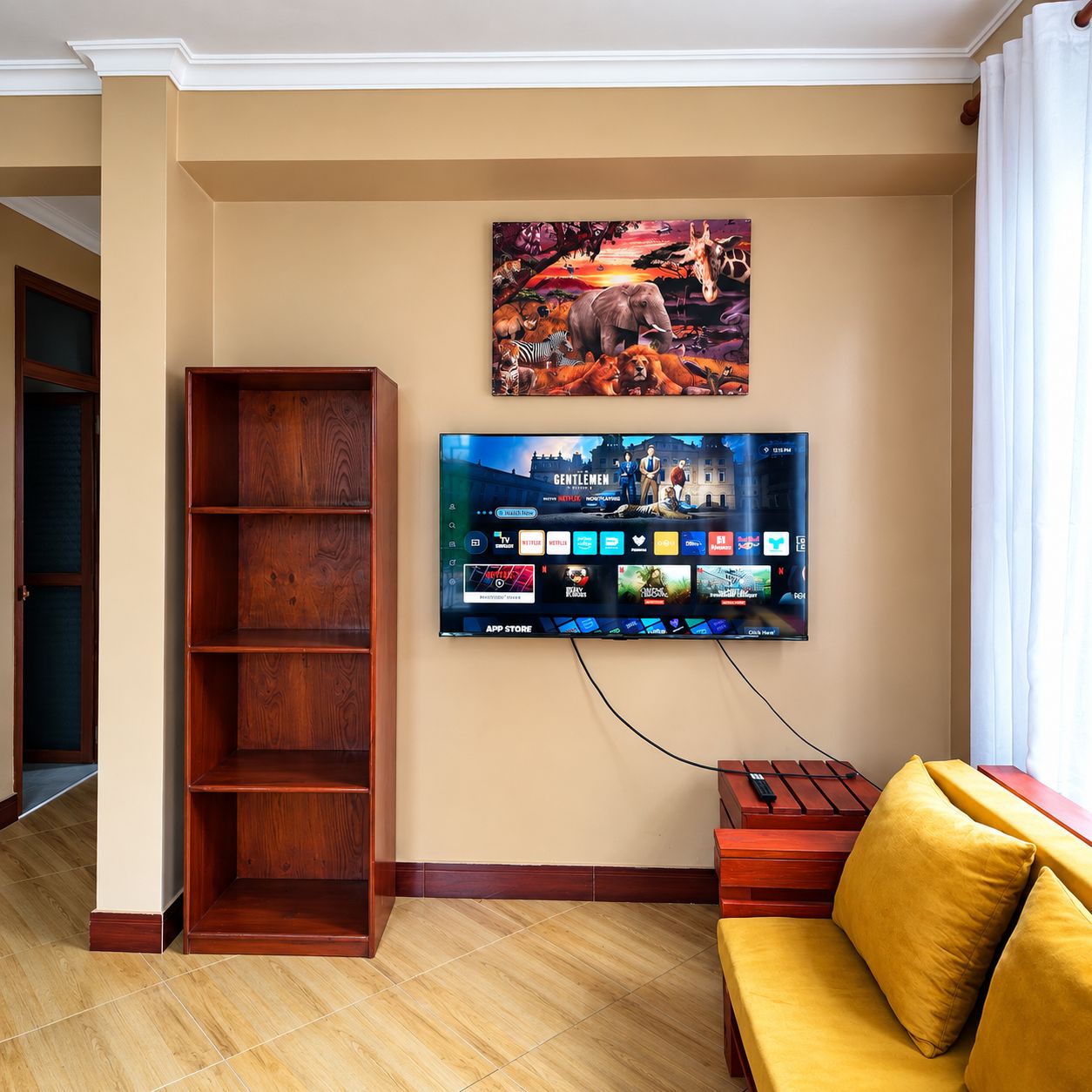 Un salon avec un téléviseur à écran plat fixé au mur, une bibliothèque en bois, un canapé jaune et une fenêtre avec des rideaux.