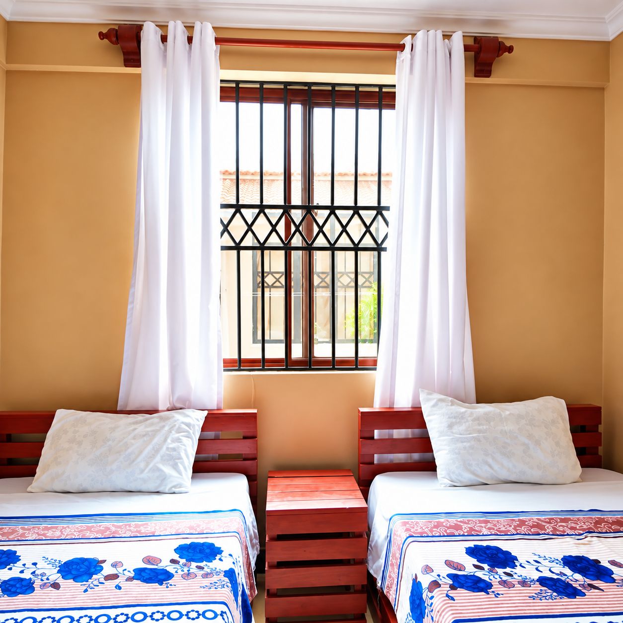 A room with two beds, a window with bars, and a view of the outside.