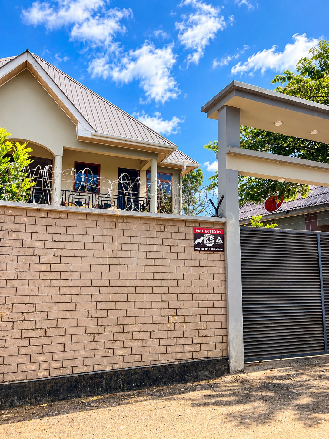 A brick wall with a security sign, a metal gate, and a building with a sloped roof.