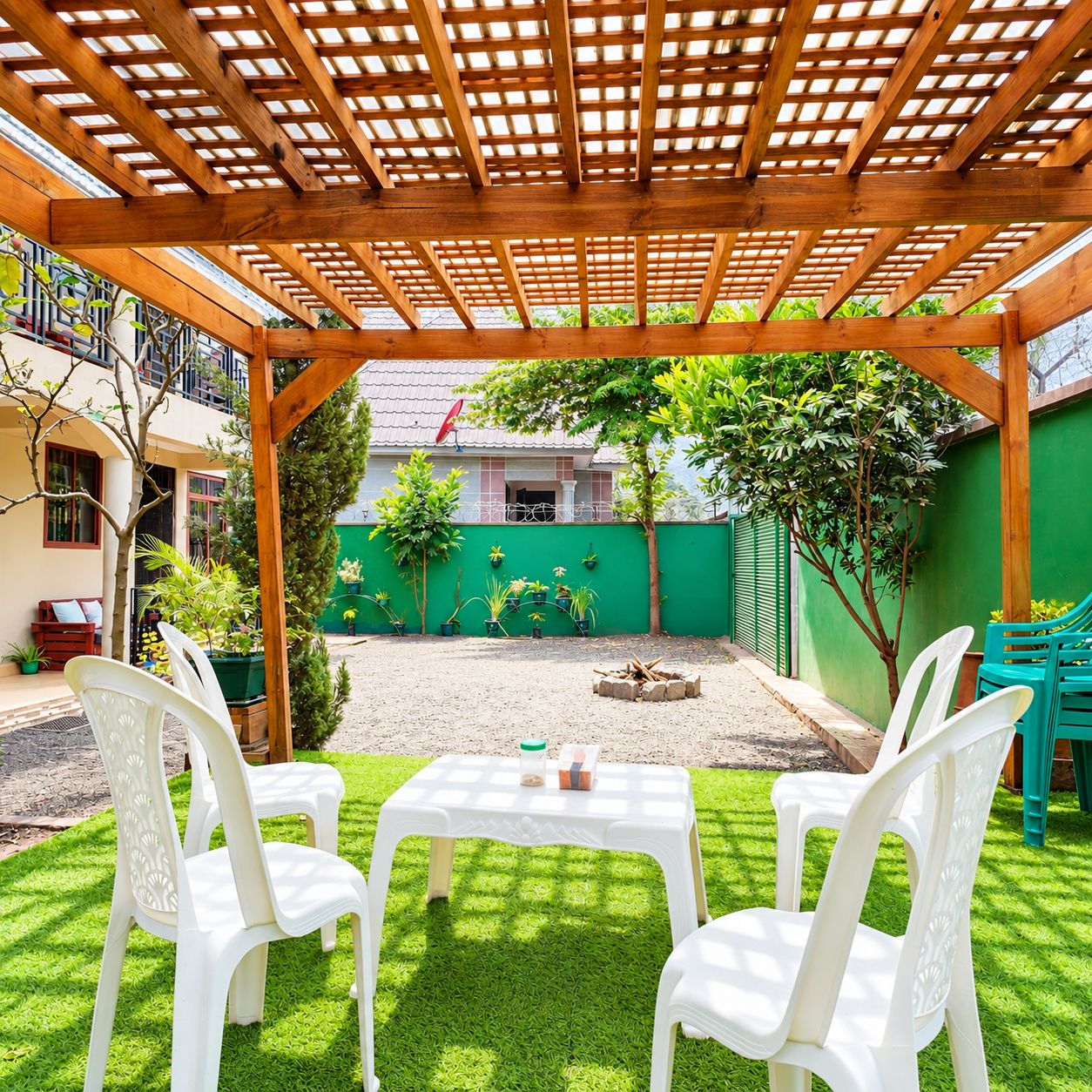 Une terrasse couverte avec une pergola en bois, deux chaises en plastique blanches, une petite table et un mur végétal agrémenté de plantes en pot.