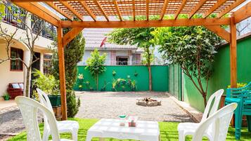 Une terrasse couverte avec une pergola en bois, deux chaises en plastique blanches, une petite table et un mur végétal agrémenté de plantes en pot.