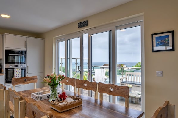 A kitchen with modern appliances, a dining area with a wooden table and chairs, and a balcony with a view of the ocean. - 23 Bayview (Phillack)