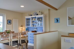 A dining area with a wooden table and chairs, a cabinet with glass doors, and a wall-mounted light fixture. - 23 Bayview (Phillack)