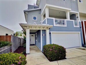 A two-story residential building with a covered entrance, a garage, and a small garden with flowering plants. - Pismo Beach House: Steps to Sand & Surf (Pismo Beach)