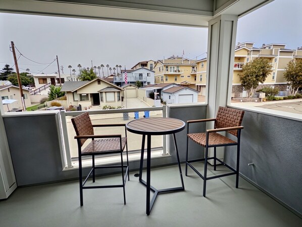 Een balkon met twee stoelen en een tafel, met uitzicht op een woonwijk met huizen en palmbomen.