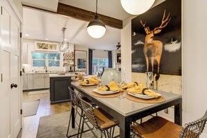 Un espace repas moderne avec une longue table, des chaises et un grand tableau représentant un cerf accroché au mur.