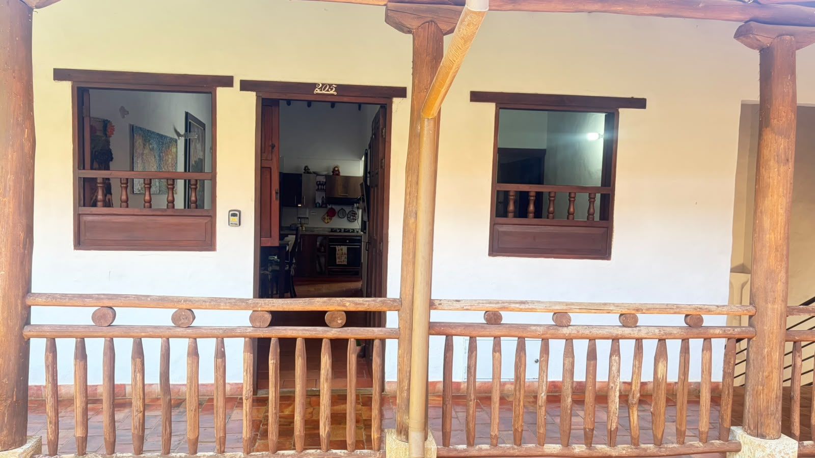 A wooden balcony with a railing, a door leading to a kitchen, and a window with a view.