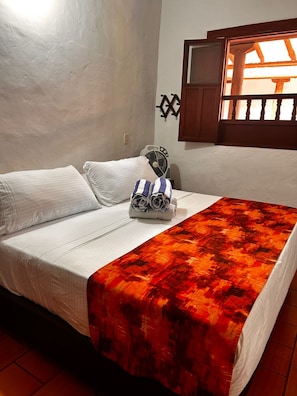 Una cama con sábanas blancas, una toalla enrollada y una colcha de cuadros rojos.