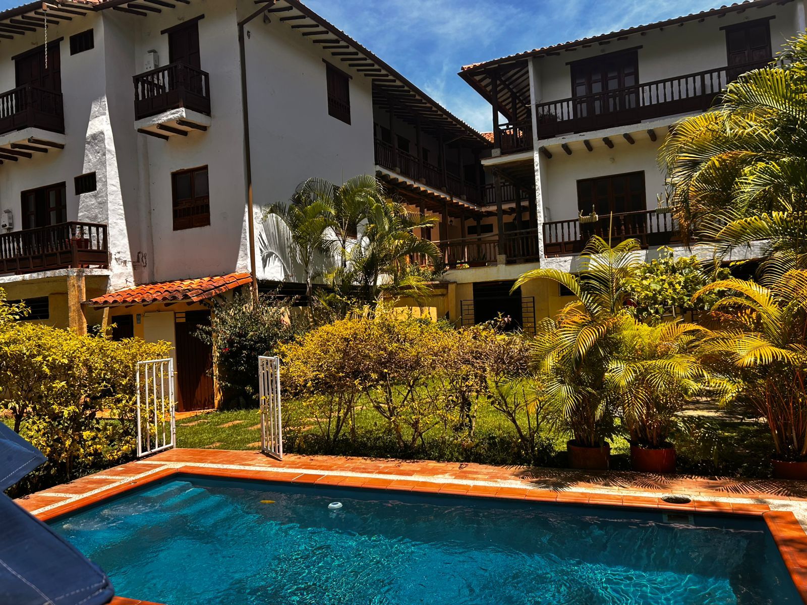 A swimming pool with a tiled edge, surrounded by lush greenery and a multi-story building with balconies.