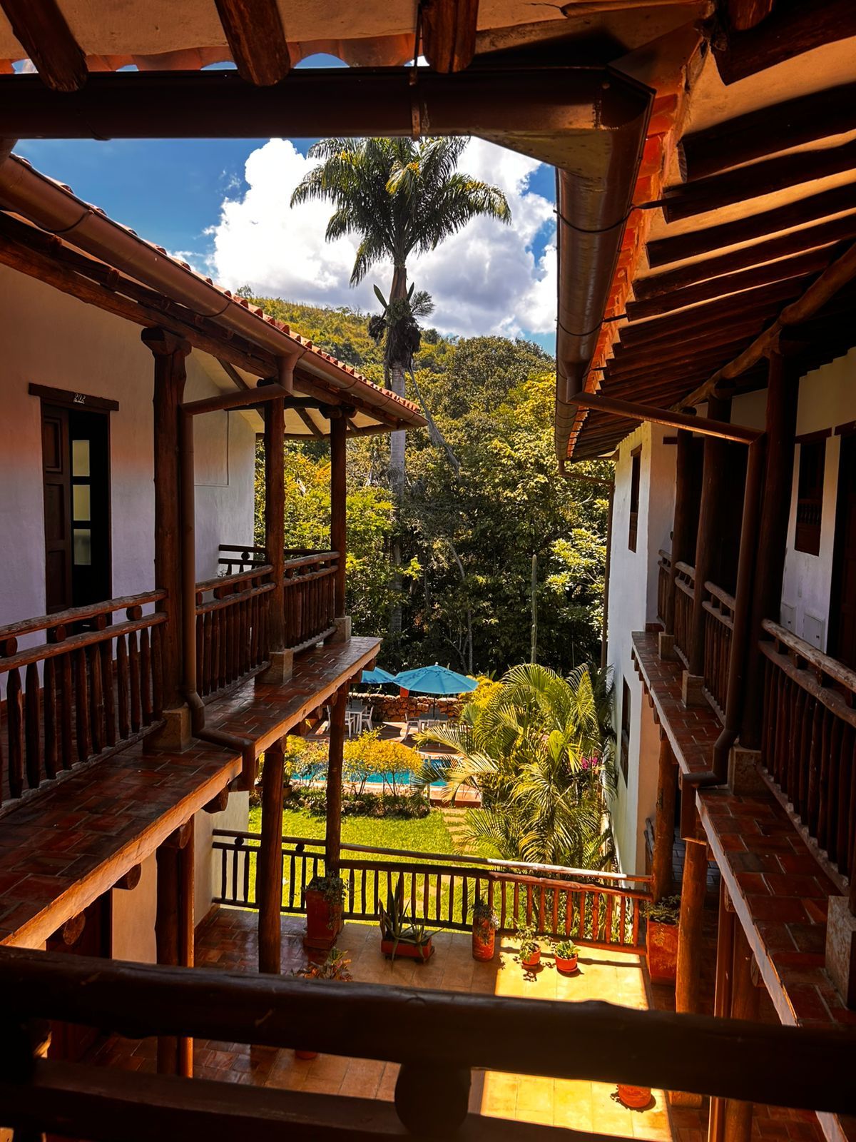 A balcony with wooden railings overlooking a pool and lush greenery.