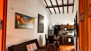 A cozy living room with a sofa and a painting, a kitchen with modern appliances, and a dining area with chairs.