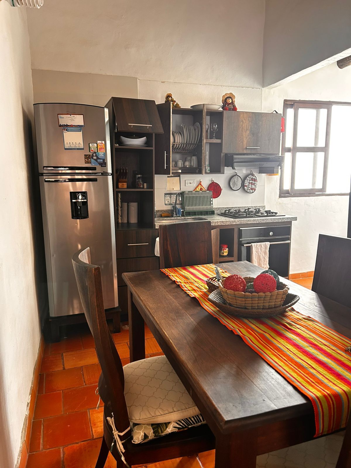 Una cocina con refrigerador, estufa y mesa de comedor con sillas.
