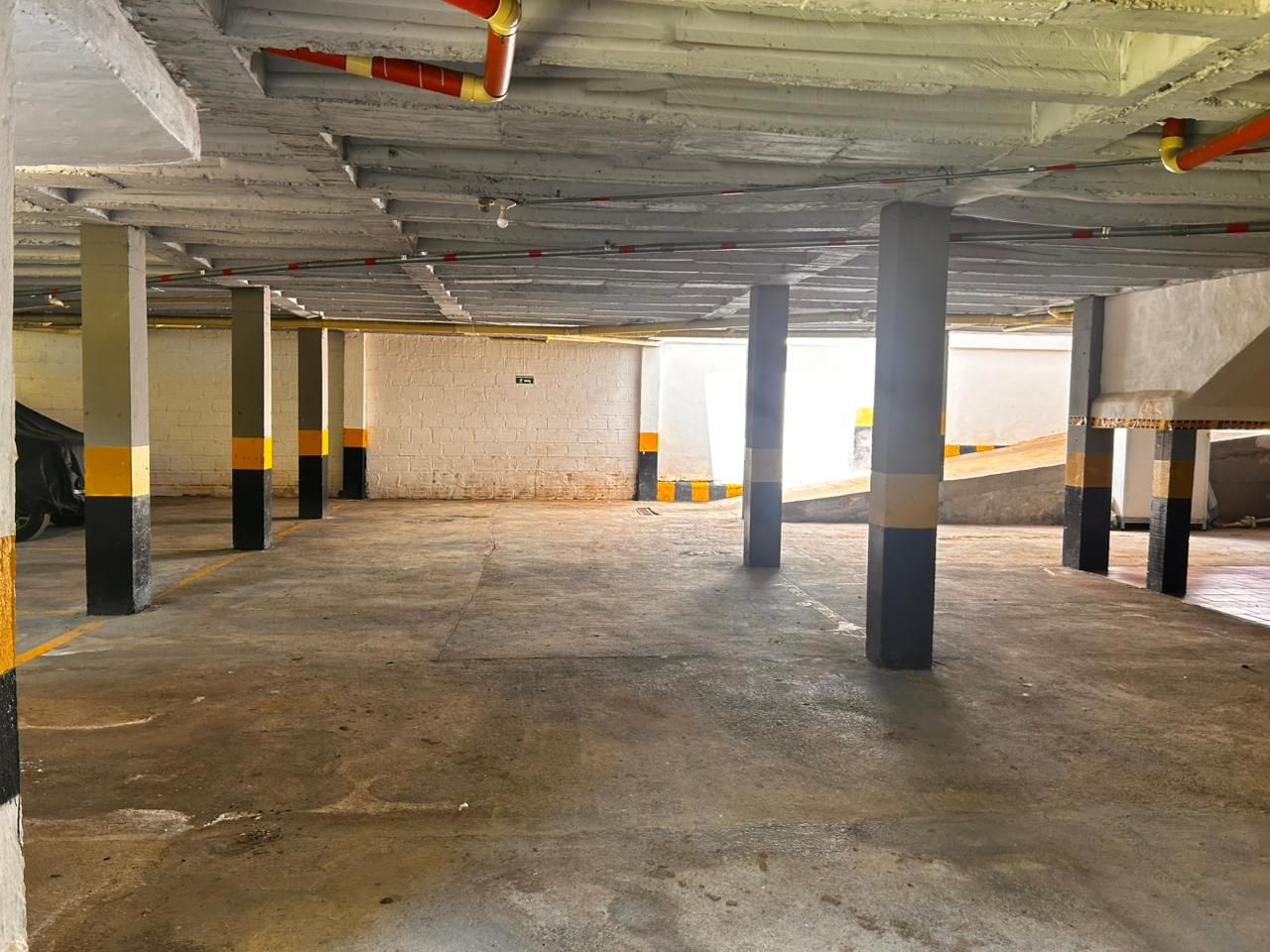 An indoor parking garage with concrete floors and pillars, some with yellow and black stripes.