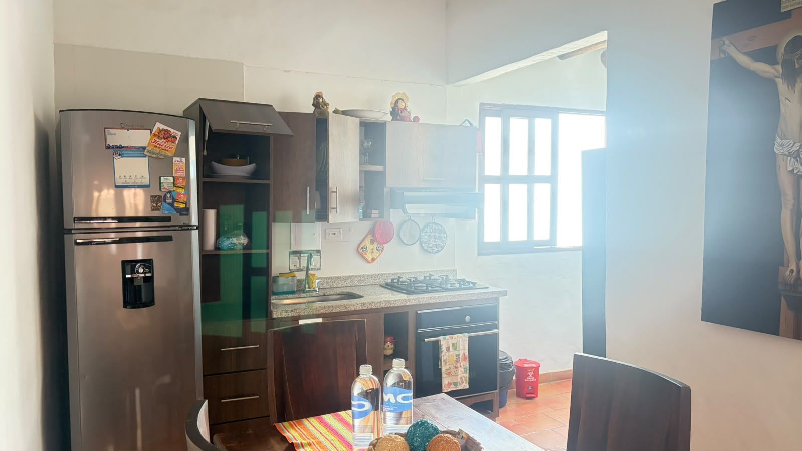 Cocina compacta con refrigerador, lavamanos y estufa. Hay armarios y una ventana que proporciona luz natural.