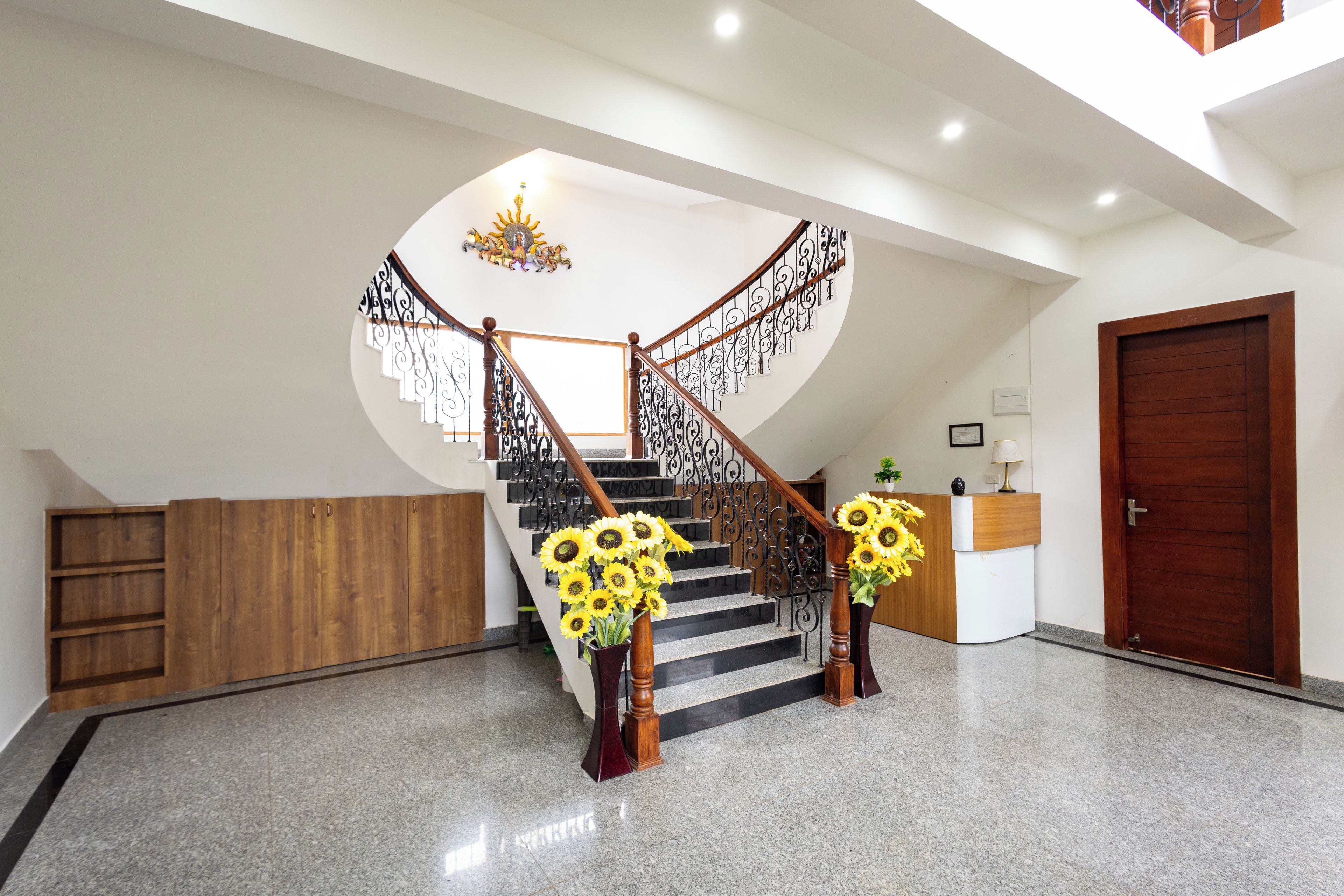A staircase with a wooden handrail and black balusters, leading to a landing with a chandelier.