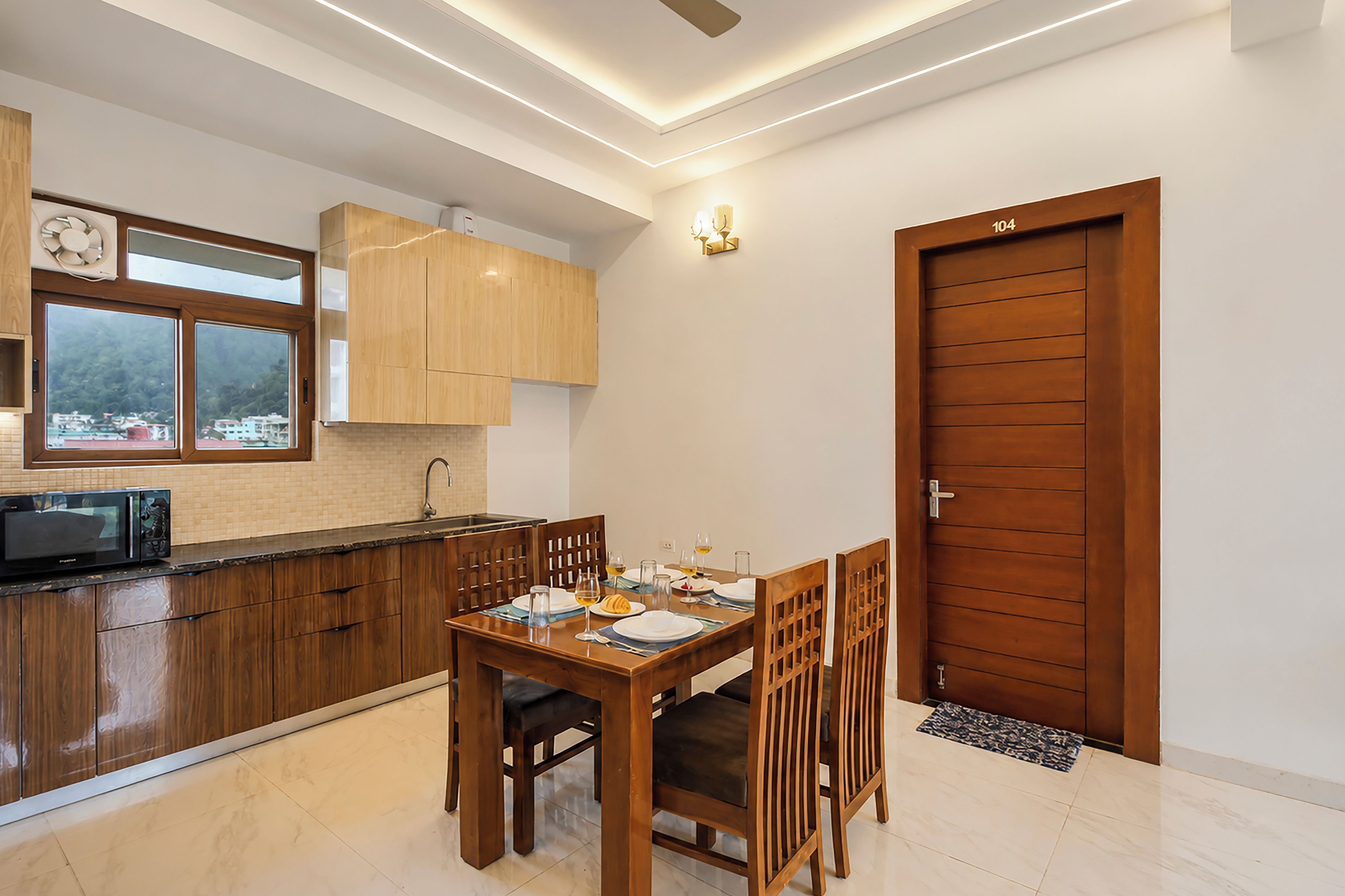 Une cuisine moderne avec des meubles en bois, une table à manger dressée pour deux personnes et une vue par la fenêtre.