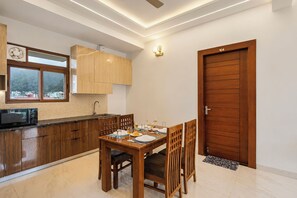 A modern kitchen with wooden cabinets, a dining table set for two, and a view through a window. - Alaya Stays Key Shree Bhawan 2BHK Apt (Bhowali Range)