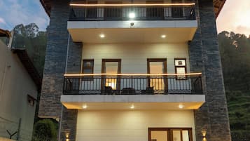 A two-story building with a balcony on the upper floor, a garage entrance, and a series of potted plants in front.