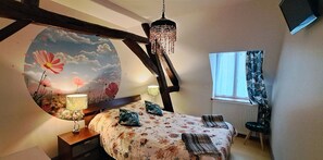 A bedroom with a bed, two bedside lamps, a hanging chandelier, a window with curtains, and a wall mural. - domaine de montboulon  (Perrigny)