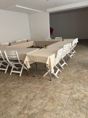 Une salle de conférence avec une longue table, des chaises blanches et un sol carrelé.