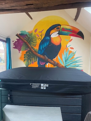 A room with a mural of a toucan on the wall, a window with blue curtains, and a black sofa.