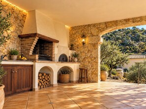 An outdoor kitchen with a brick oven, stone walls, and a view of the surrounding landscape. - Romantic designed stone house with pool & views (Palau-Saverdera)