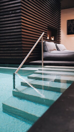 Ein moderner Poolbereich mit Metallhandlauf, grauem Sofa und einer Wand aus Holzlatten.