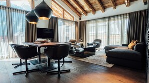 Una sala de estar moderna con techo de madera, un comedor con mesa y sillas, y un sofá con vistas a las montañas.