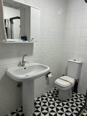 Ein Badezimmer mit weißem Waschbecken, Toilette und Fliesenboden.
