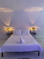 Habitación con una cama individual, colcha blanca, dos lámparas de noche y un par de toallas dobladas sobre la cama.