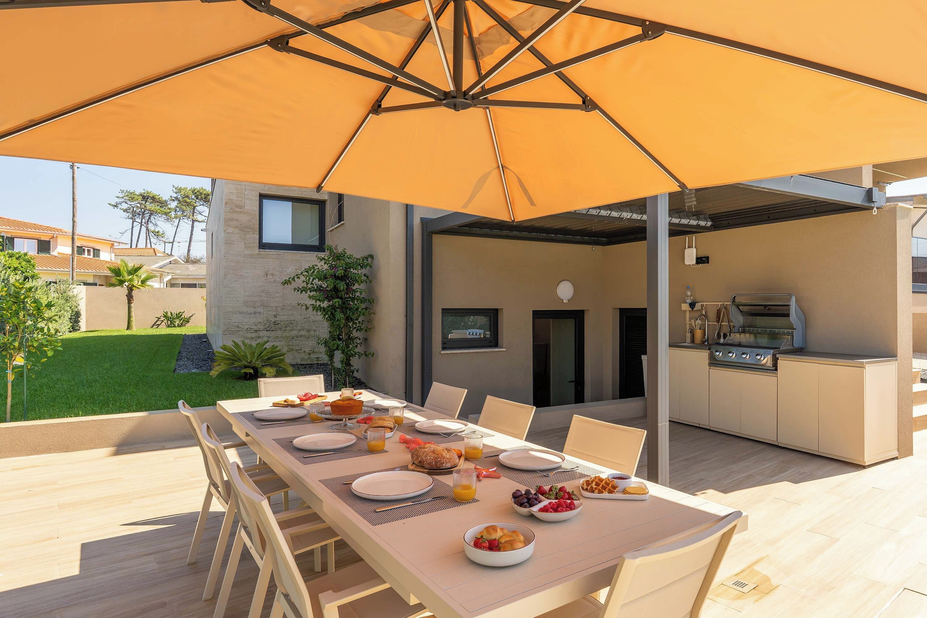 Un área de comedor al aire libre con mesa lista para el desayuno, una parrilla y vistas del vecindario.
